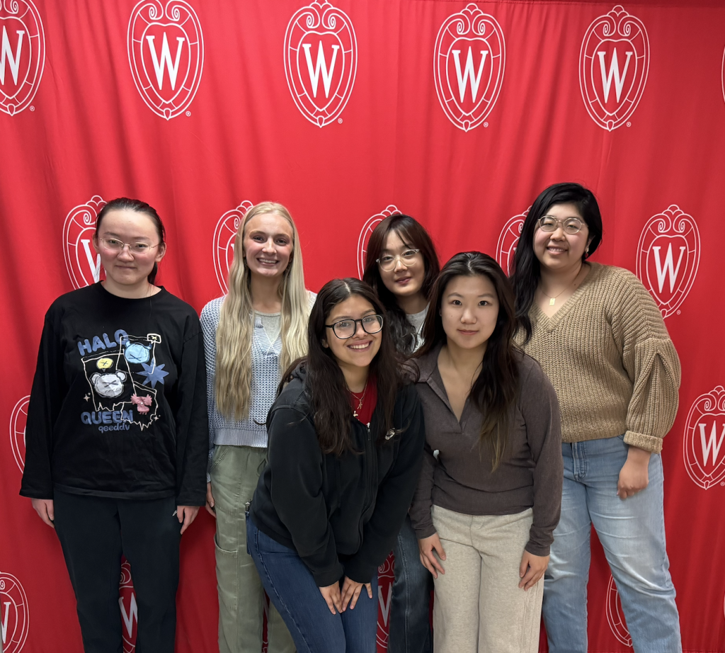 Social and Moral Learning Lab members and principal investigator Dr. Pearl Han Li posing together in front of a red UW–Madison backdrop.